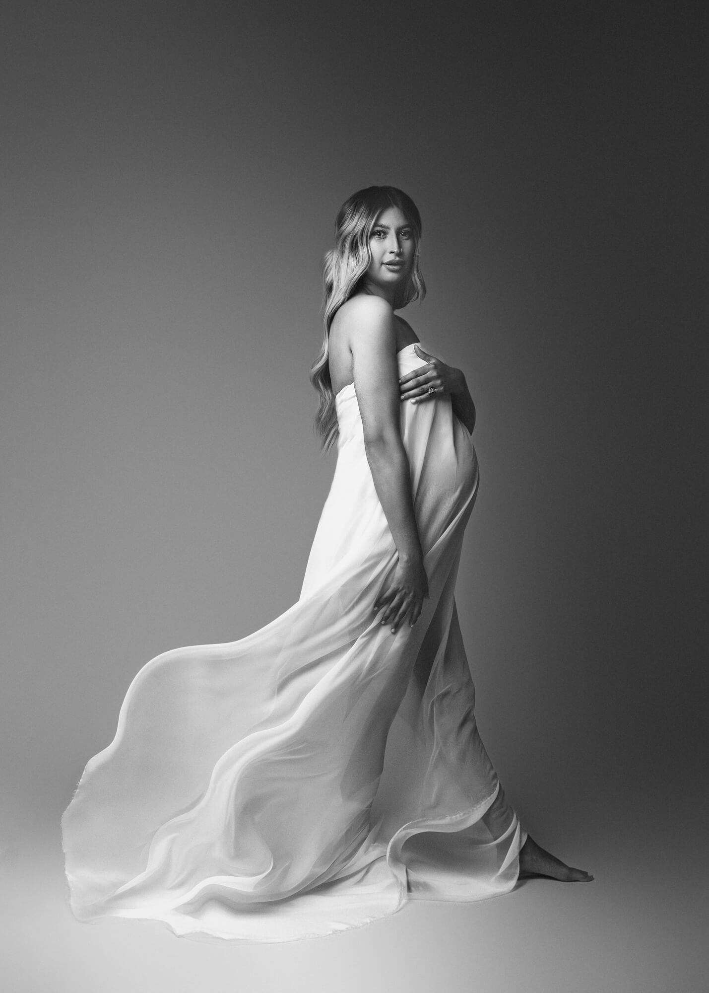 Maternity session in Fresno studio with mom wearing elegant white silk drapery by Roxy G Photography.